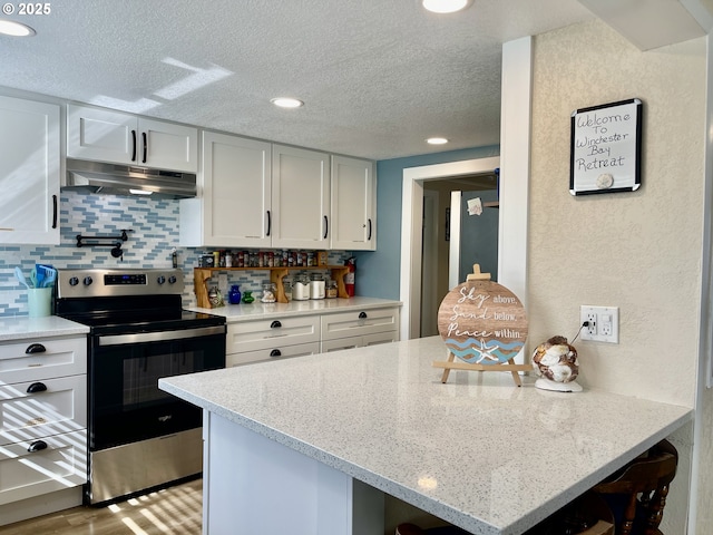 kitchen featuring electric range, decorative backsplash, a textured ceiling, under cabinet range hood, and a peninsula