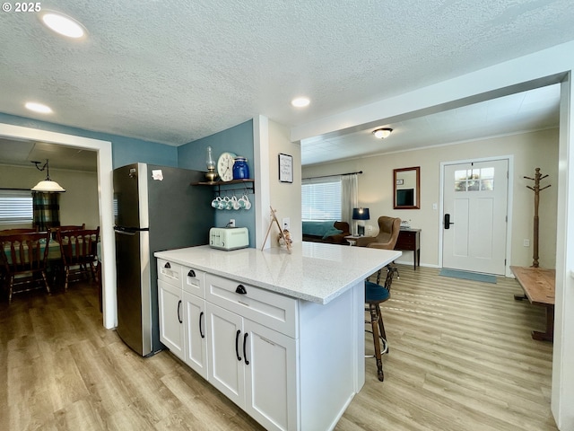 kitchen with light wood-style floors, freestanding refrigerator, white cabinetry, light stone countertops, and a kitchen breakfast bar