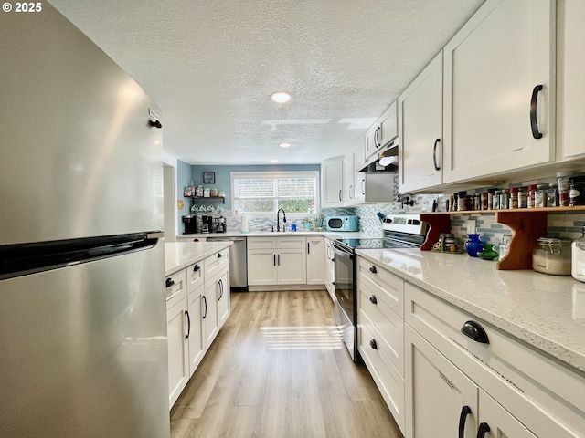 kitchen with under cabinet range hood, stainless steel appliances, light wood-style floors, white cabinets, and light stone countertops