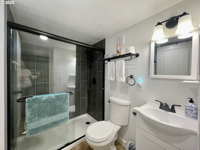 full bathroom with a textured ceiling, a textured wall, toilet, vanity, and a shower stall