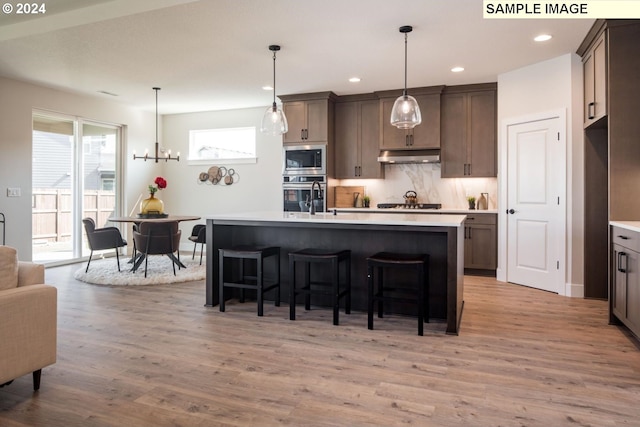 kitchen with hanging light fixtures, hardwood / wood-style floors, an island with sink, and stainless steel appliances