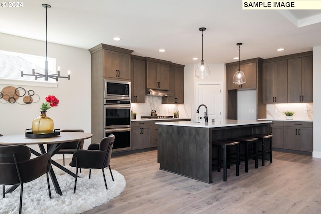 kitchen featuring decorative light fixtures, stainless steel appliances, light hardwood / wood-style floors, and an island with sink