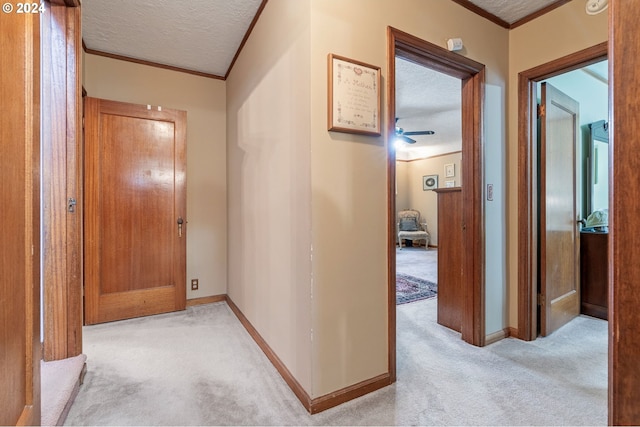 hallway with light colored carpet, a textured ceiling, and ornamental molding