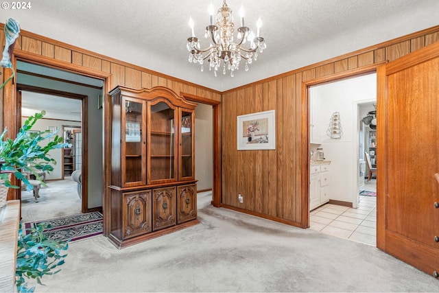 interior space featuring a textured ceiling, wood walls, light carpet, and a notable chandelier