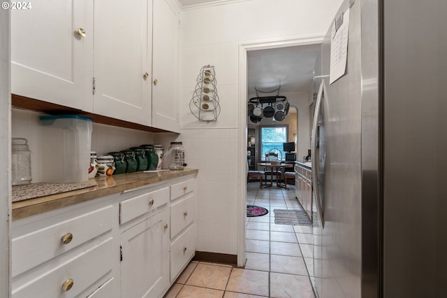 kitchen with ornamental molding, white cabinetry, light tile patterned flooring, and stainless steel fridge