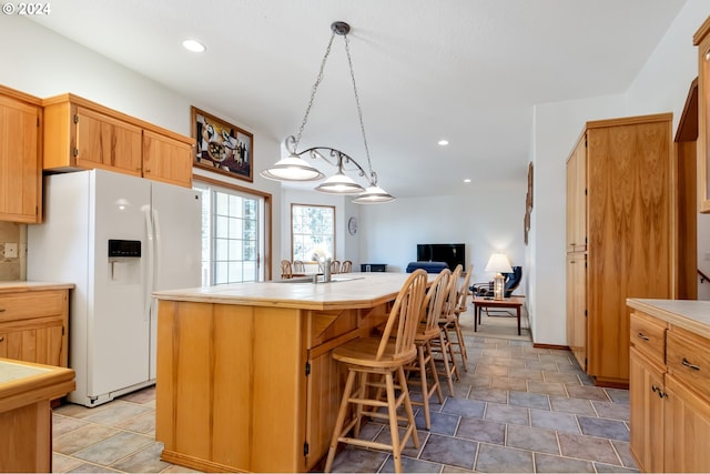 kitchen featuring a kitchen island, a kitchen bar, decorative light fixtures, tile counters, and white fridge with ice dispenser