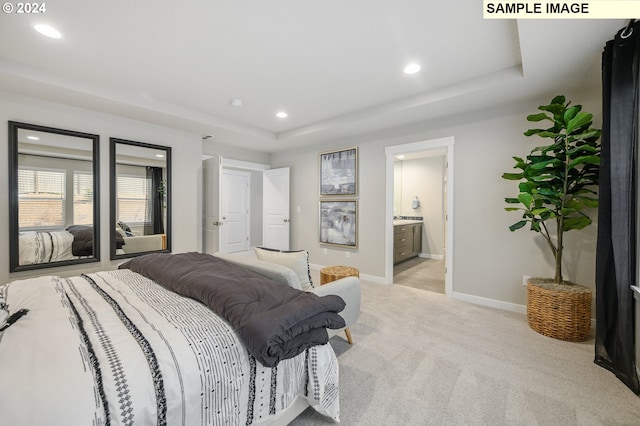 bedroom with ensuite bathroom, a raised ceiling, and light colored carpet