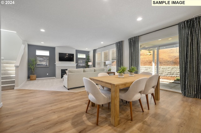 dining room featuring a tiled fireplace, light hardwood / wood-style floors, and a textured ceiling