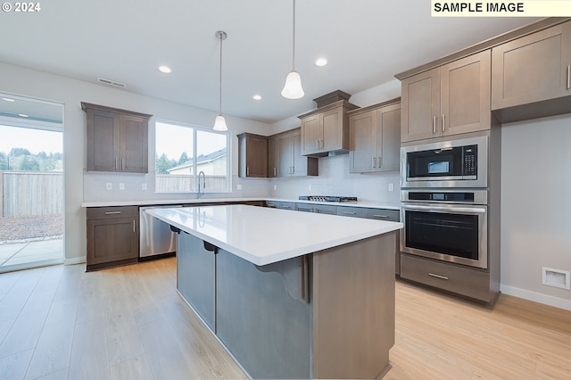 kitchen featuring a kitchen island, a breakfast bar, light hardwood / wood-style floors, appliances with stainless steel finishes, and decorative light fixtures