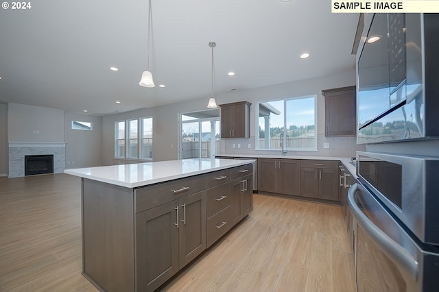 kitchen featuring light hardwood / wood-style floors, a kitchen island, backsplash, a fireplace, and hanging light fixtures