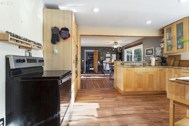 kitchen with light stone countertops, light brown cabinetry, light wood-type flooring, black range with electric cooktop, and ceiling fan