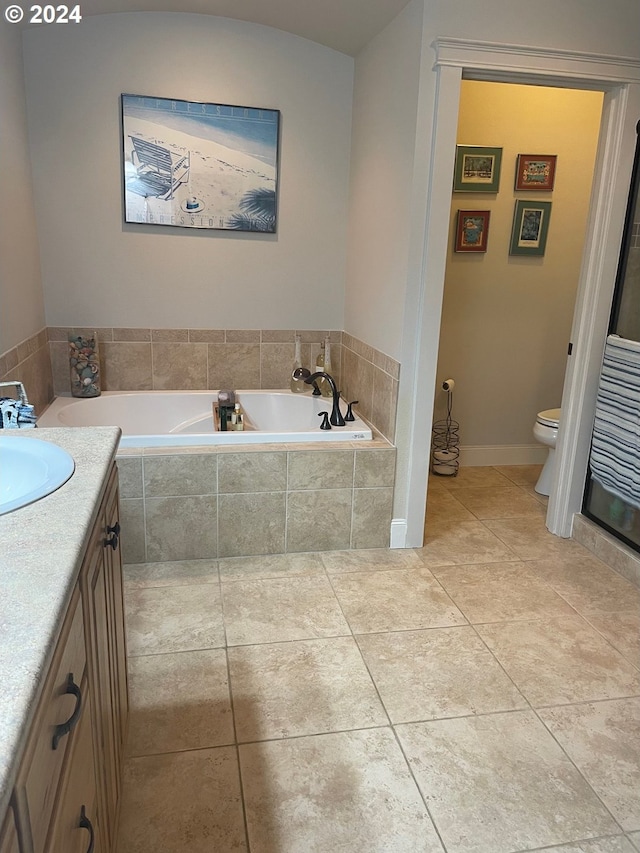 bathroom with tile patterned floors, vanity, a relaxing tiled tub, and toilet