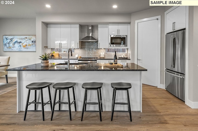 kitchen with light wood-type flooring, wall chimney exhaust hood, stainless steel appliances, sink, and white cabinets