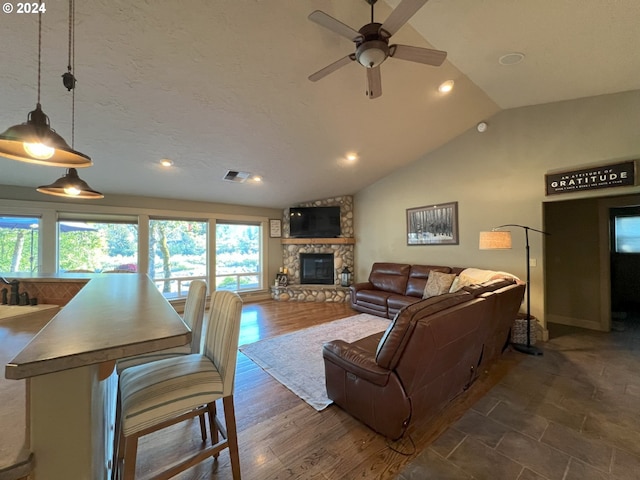 living room with dark hardwood / wood-style floors, a stone fireplace, ceiling fan, and lofted ceiling