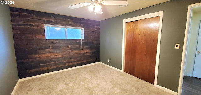 unfurnished bedroom with carpet flooring, ceiling fan, wood walls, and a closet