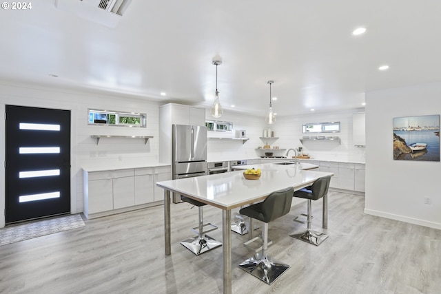 kitchen with pendant lighting, white cabinets, a large island with sink, stainless steel refrigerator, and light wood-type flooring