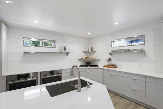 kitchen featuring light hardwood / wood-style floors, light stone countertops, sink, and stainless steel oven