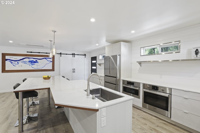 kitchen featuring an island with sink, a barn door, pendant lighting, stainless steel appliances, and sink