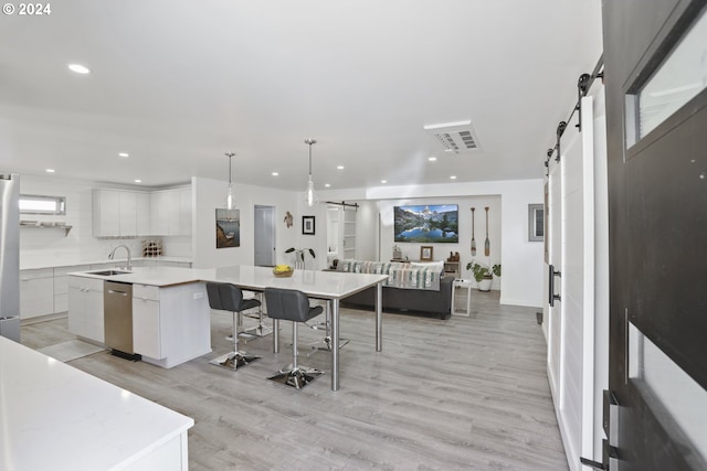 kitchen featuring light wood-type flooring, white cabinets, hanging light fixtures, a barn door, and a spacious island