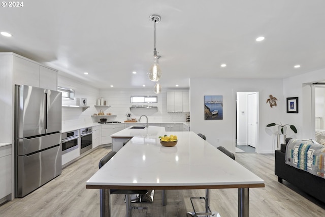 kitchen with appliances with stainless steel finishes, light hardwood / wood-style floors, white cabinetry, pendant lighting, and sink