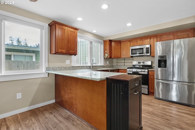 kitchen with sink, kitchen peninsula, stainless steel appliances, light stone countertops, and light hardwood / wood-style floors