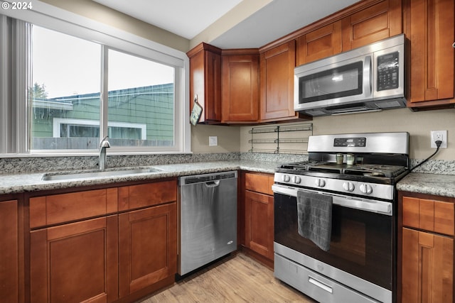 kitchen with appliances with stainless steel finishes, light stone countertops, sink, and light hardwood / wood-style floors