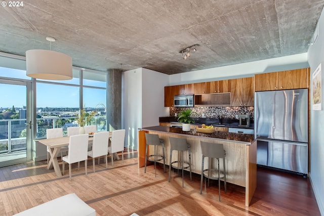 kitchen with hanging light fixtures, dark hardwood / wood-style floors, stainless steel appliances, decorative backsplash, and a kitchen breakfast bar