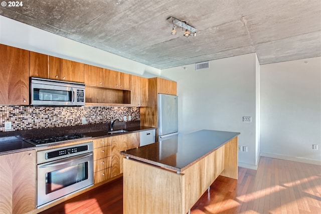 kitchen with appliances with stainless steel finishes, dark wood-type flooring, a kitchen island, sink, and backsplash