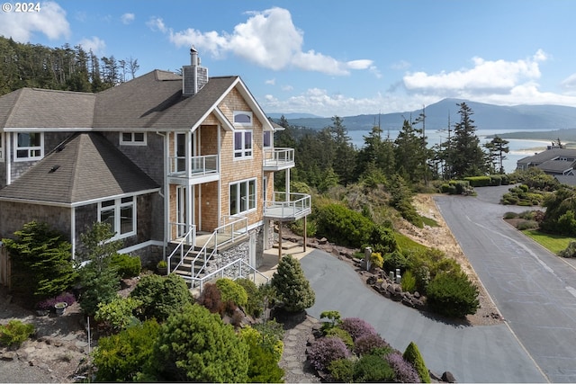 exterior space featuring a chimney, a shingled roof, a mountain view, a balcony, and driveway