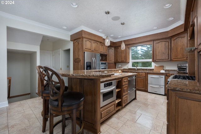 kitchen with brown cabinetry, dark stone counters, a kitchen island, stainless steel appliances, and a kitchen bar