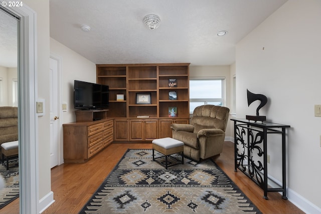 sitting room with light wood-style floors, a textured ceiling, and baseboards