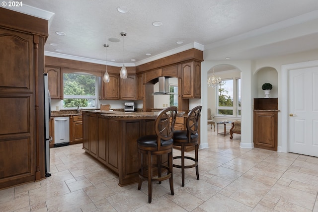 kitchen with pendant lighting, wall chimney exhaust hood, appliances with stainless steel finishes, a wealth of natural light, and a center island