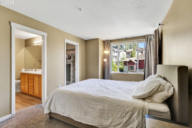 bedroom with light hardwood / wood-style floors, a closet, a textured ceiling, a walk in closet, and ensuite bathroom