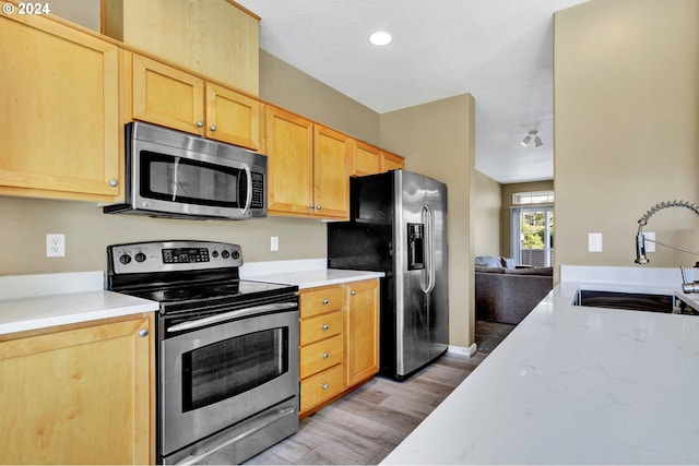 kitchen featuring light brown cabinets, sink, a textured ceiling, stainless steel appliances, and light wood-type flooring