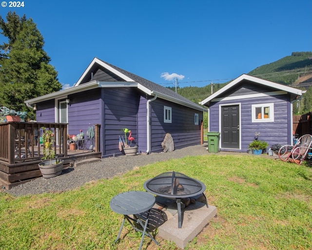 back of house with a shed, an outdoor fire pit, a deck, and a yard