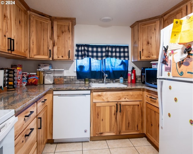 kitchen with sink, dark stone counters, white appliances, and light tile floors