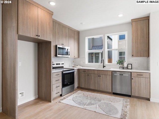 kitchen with backsplash, sink, stainless steel appliances, and light wood-type flooring