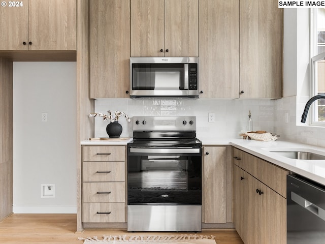 kitchen with light brown cabinets, backsplash, sink, light hardwood / wood-style flooring, and appliances with stainless steel finishes