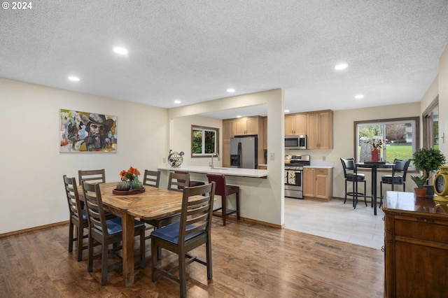 dining room featuring sink, a textured ceiling, and light hardwood / wood-style floors