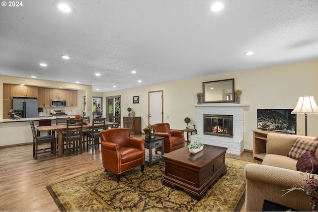 living room with a brick fireplace, a textured ceiling, and light hardwood / wood-style floors