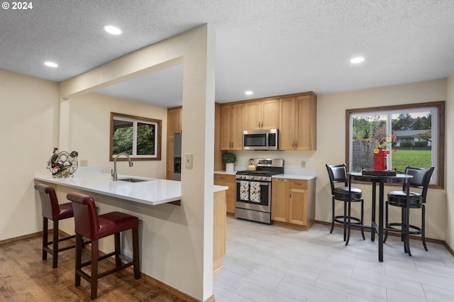 kitchen with kitchen peninsula, a breakfast bar area, appliances with stainless steel finishes, a textured ceiling, and sink