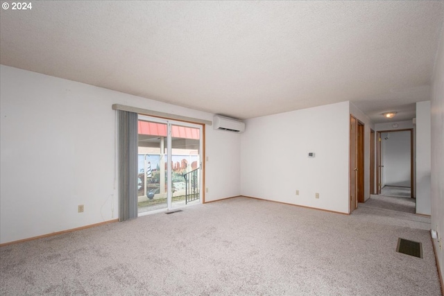 spare room with an AC wall unit, a textured ceiling, and carpet