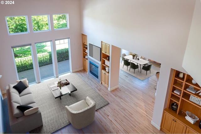 living room with baseboards, a tile fireplace, a high ceiling, and light wood-style floors