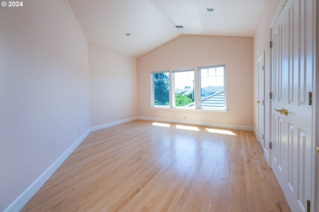 spare room featuring baseboards, vaulted ceiling, and light wood finished floors