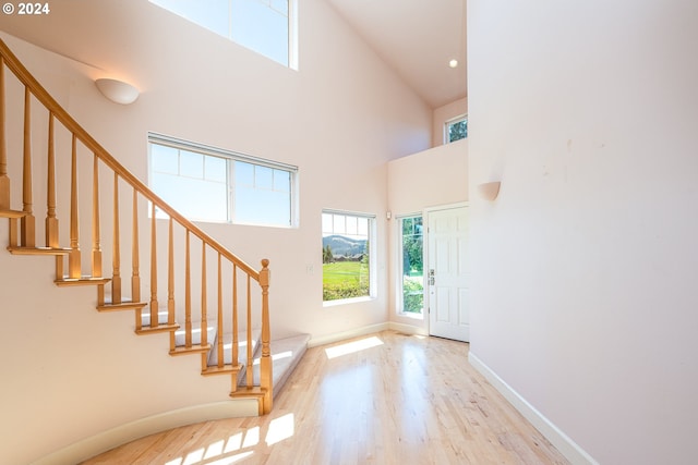 living room featuring light wood-style flooring, a towering ceiling, and baseboards