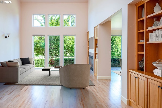 living area with a glass covered fireplace, light wood-type flooring, a towering ceiling, and baseboards