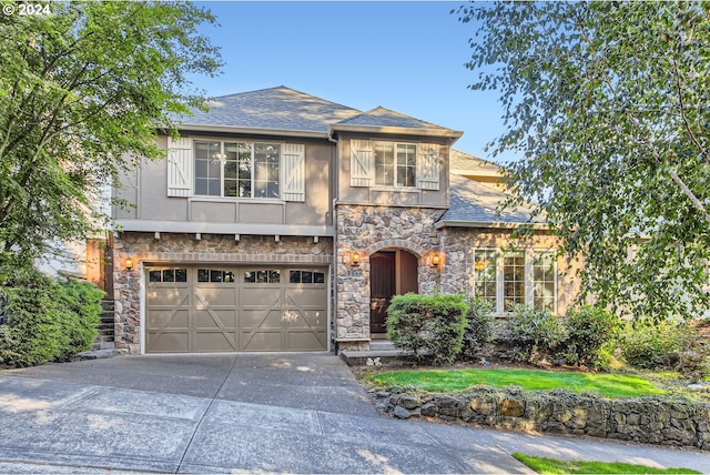 view of front facade featuring an attached garage, a shingled roof, driveway, stone siding, and stucco siding