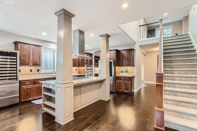 kitchen featuring arched walkways, ornate columns, island range hood, and open shelves