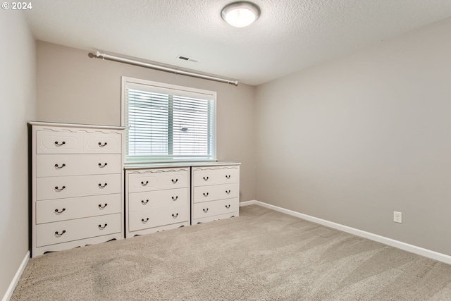 unfurnished bedroom featuring light carpet, a textured ceiling, visible vents, and baseboards