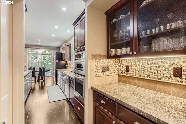 kitchen featuring stainless steel double oven, tasteful backsplash, glass insert cabinets, and light stone counters